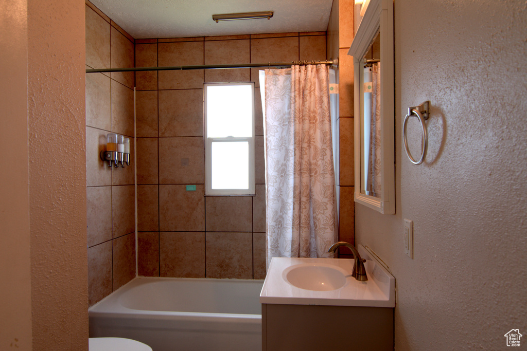 Full bathroom with a textured ceiling, shower / tub combo, toilet, and vanity with extensive cabinet space