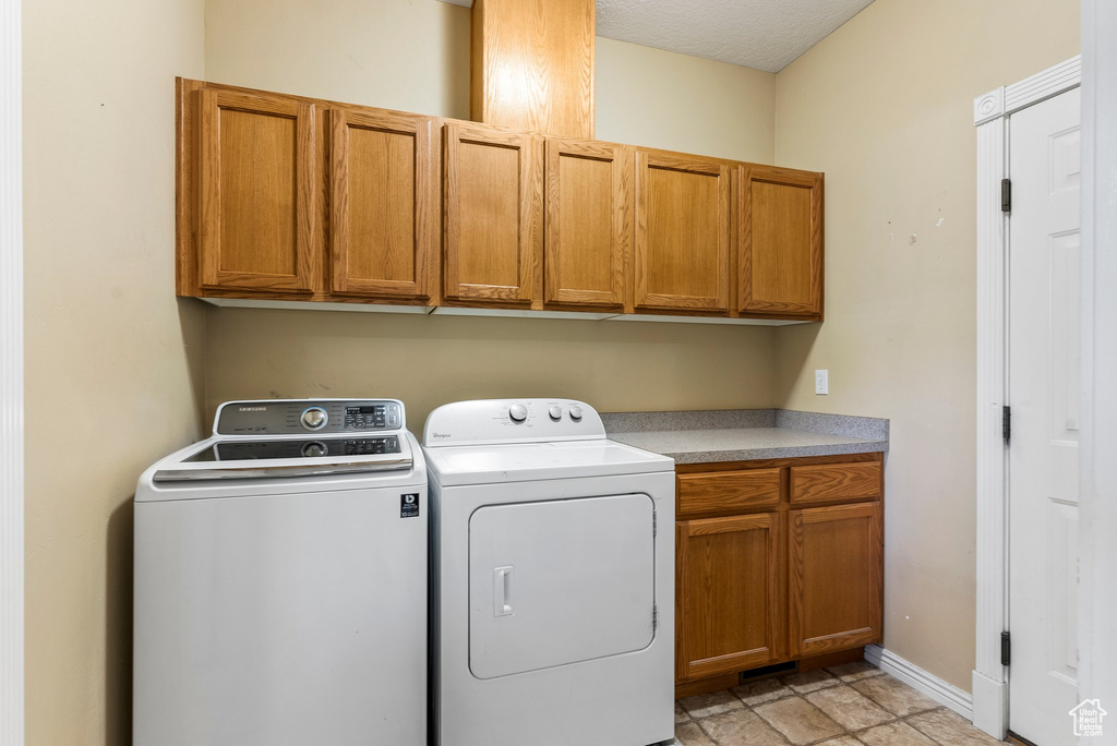 Laundry area with washing machine and dryer, light tile flooring, and cabinets