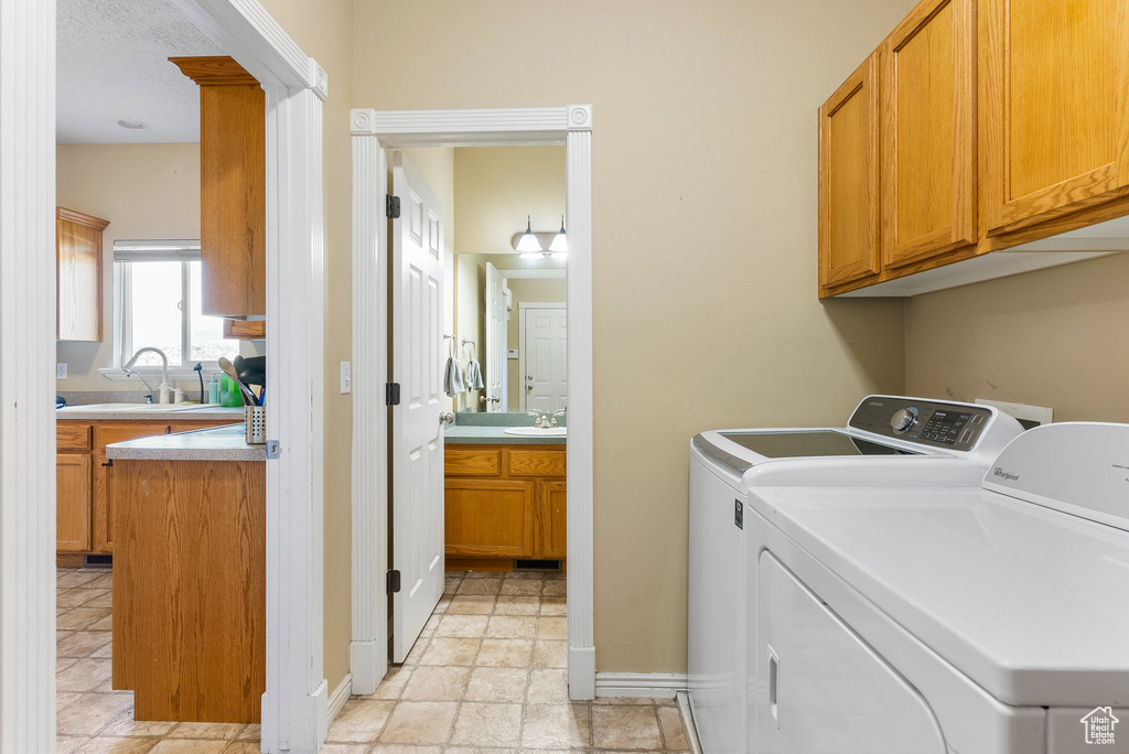 Laundry area featuring washing machine and dryer, cabinets, sink, and light tile flooring