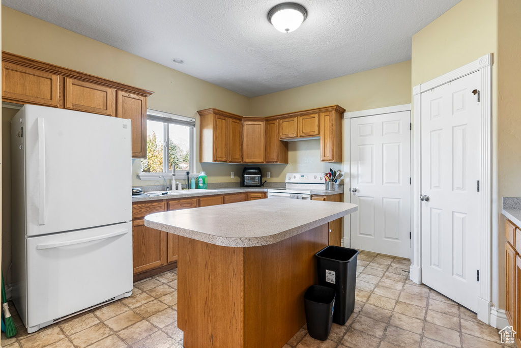 Kitchen with sink, white appliances, light tile flooring, and a center island