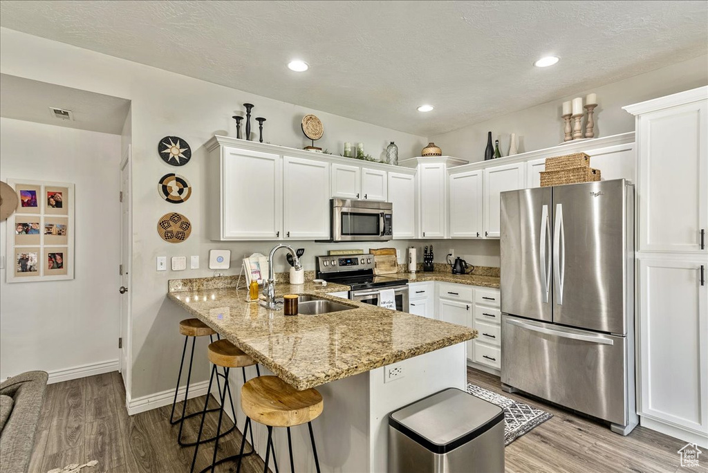 Kitchen with appliances with stainless steel finishes, light hardwood / wood-style floors, white cabinets, and a kitchen bar