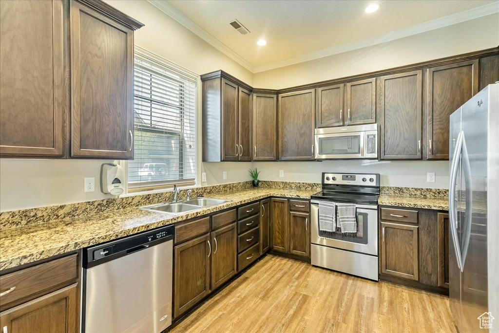 Kitchen featuring light stone counters, appliances with stainless steel finishes, sink, light wood-type flooring, and crown molding