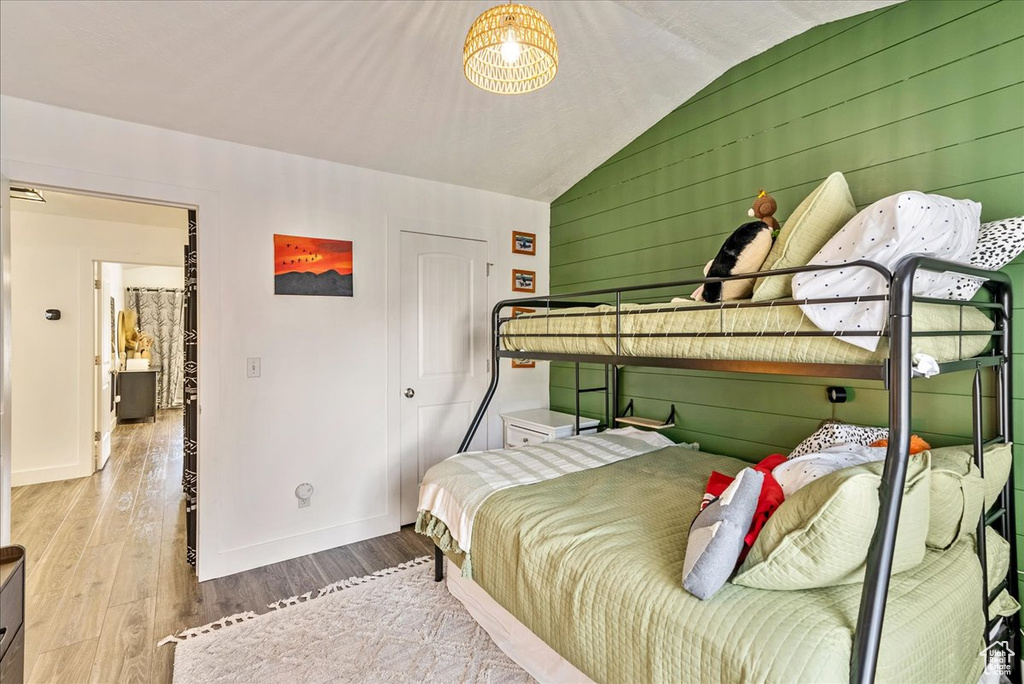Bedroom featuring wood walls, light hardwood / wood-style floors, and lofted ceiling