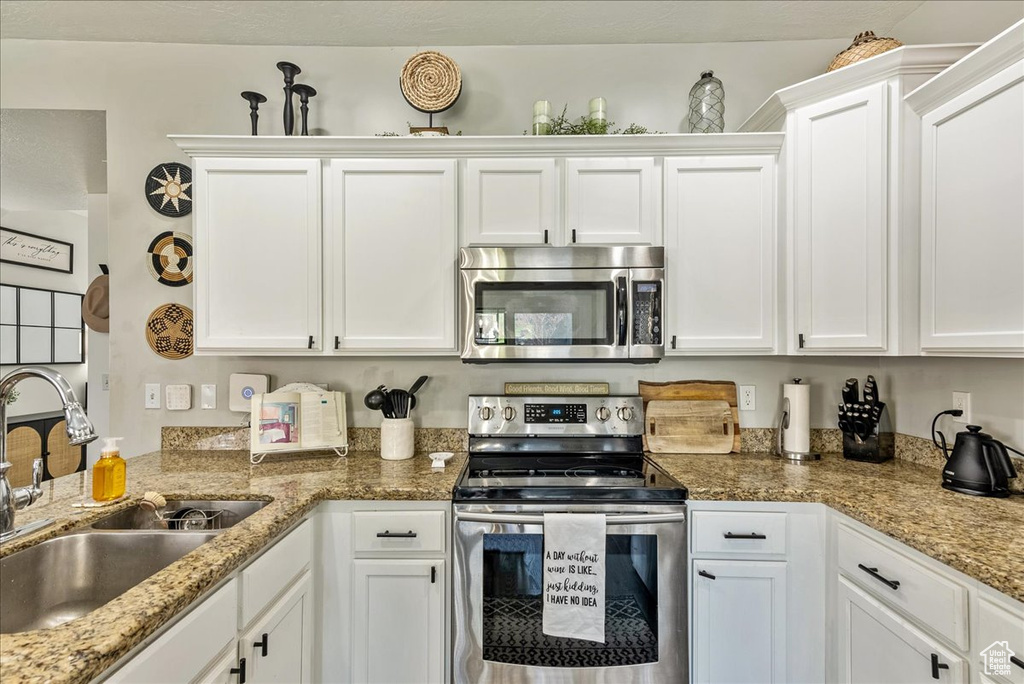 Kitchen featuring stainless steel appliances, white cabinetry, sink, and light stone countertops