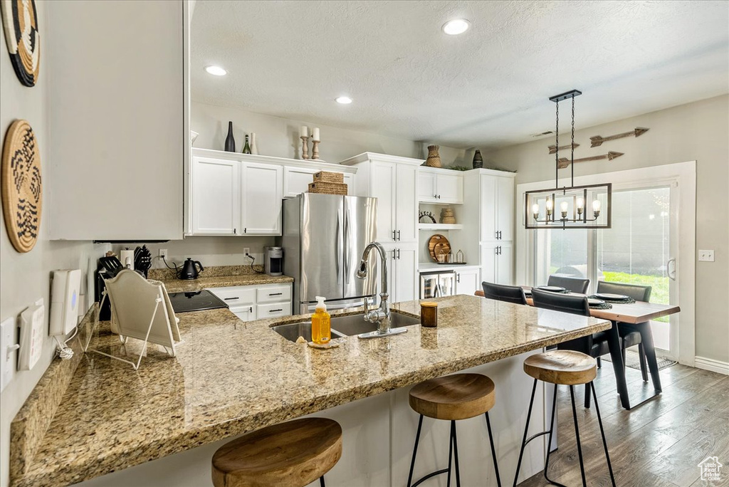 Kitchen featuring decorative light fixtures, a breakfast bar, white cabinets, stainless steel refrigerator, and light hardwood / wood-style floors