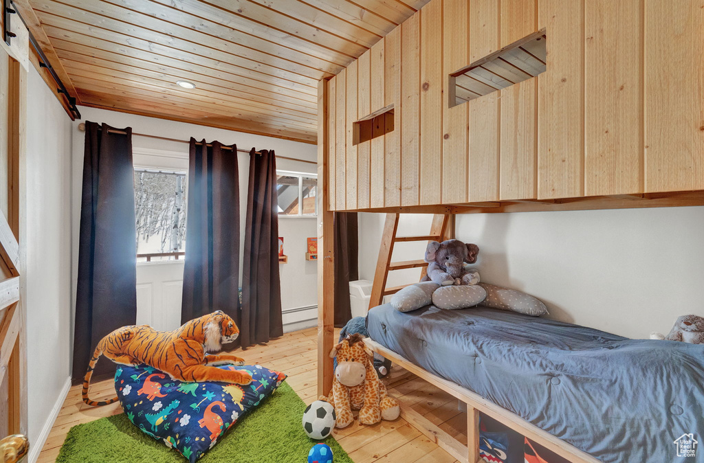 Bedroom with wood walls, light hardwood / wood-style floors, wooden ceiling, and a baseboard radiator