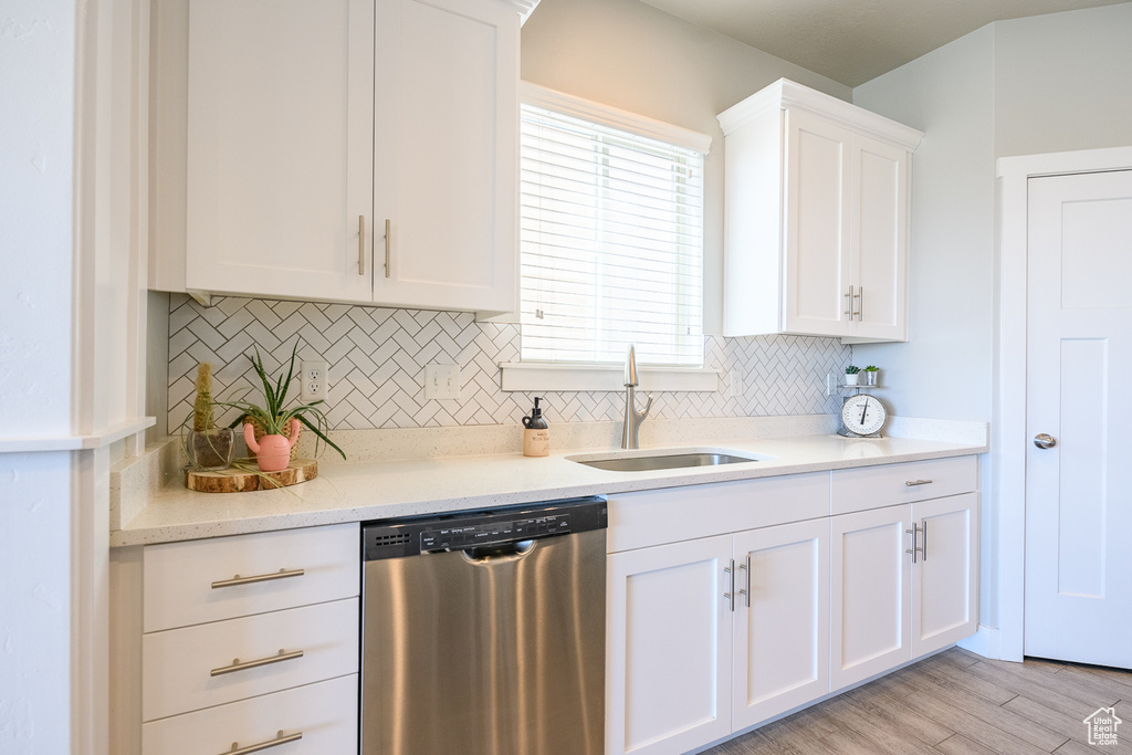 Kitchen with sink, tasteful backsplash, white cabinetry, stainless steel dishwasher, and light hardwood / wood-style flooring