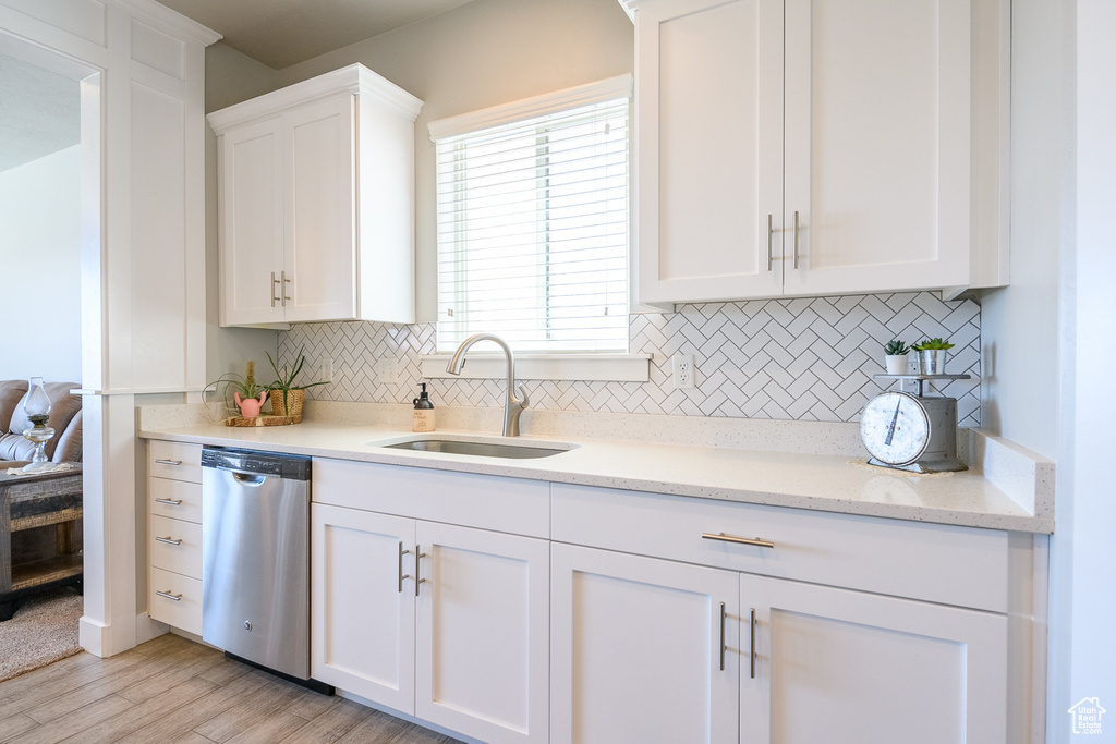 Kitchen with sink, dishwasher, tasteful backsplash, white cabinetry, and light stone countertops