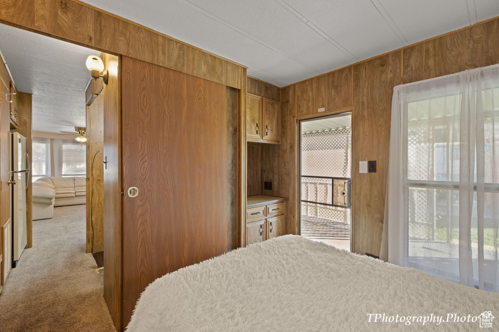 Bedroom with fridge, light colored carpet, multiple windows, and wooden walls