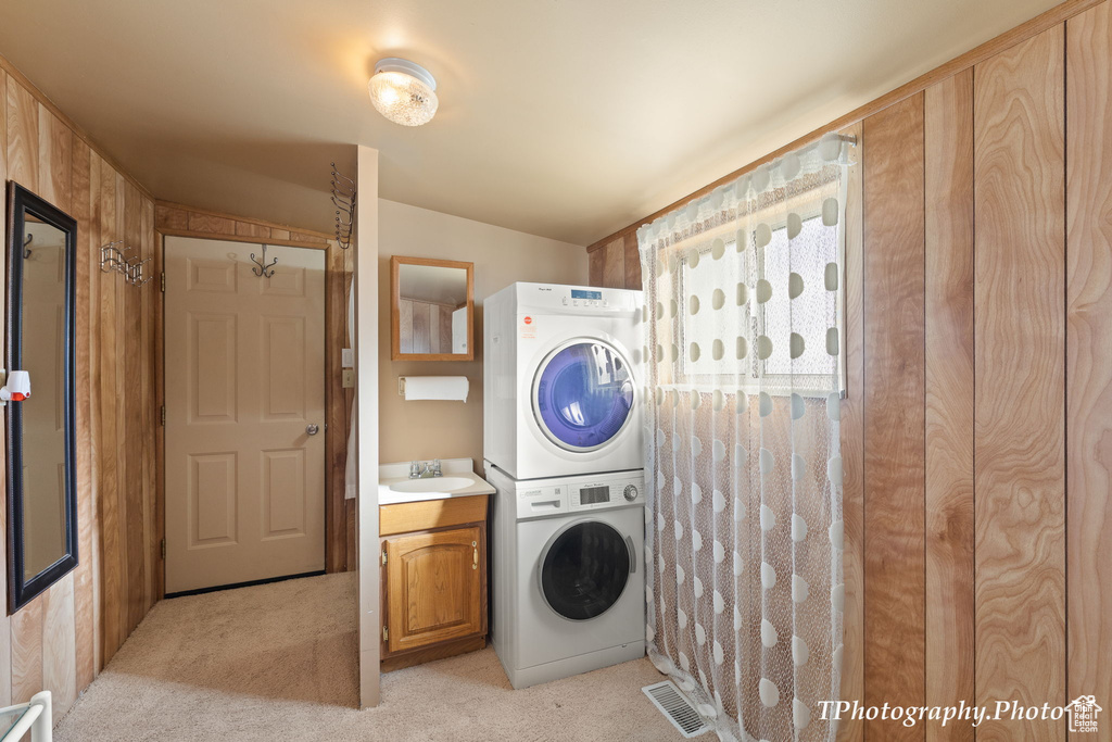 Clothes washing area with cabinets, stacked washer / dryer, light carpet, and sink