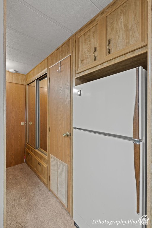 Kitchen featuring white fridge, wood walls, and light colored carpet