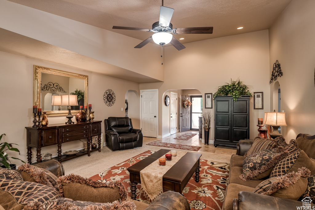 Living room featuring light colored carpet, a textured ceiling, ceiling fan, and a high ceiling