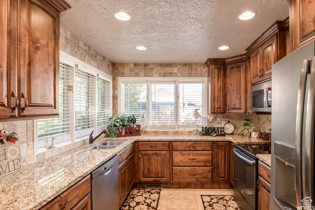 Kitchen featuring light stone countertops, light tile flooring, stainless steel appliances, sink, and a textured ceiling