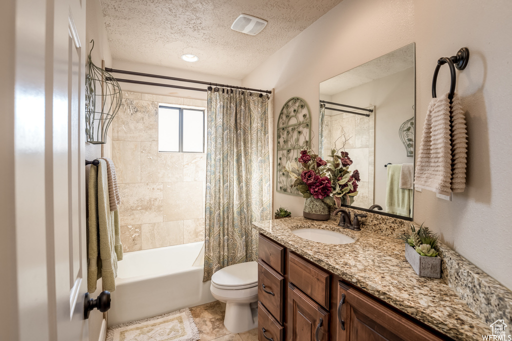 Full bathroom featuring tile flooring, vanity with extensive cabinet space, a textured ceiling, toilet, and shower / bathtub combination with curtain