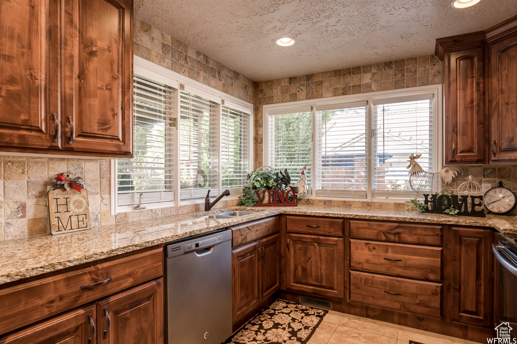 Kitchen featuring light stone counters, a textured ceiling, sink, dishwasher, and light tile flooring