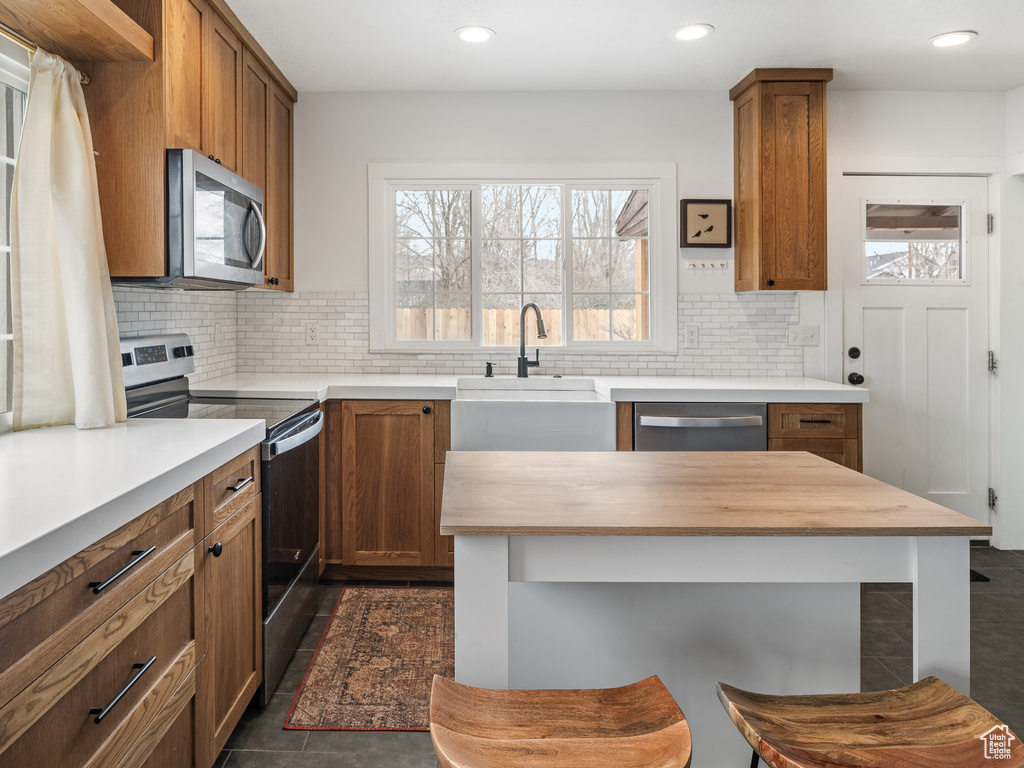 Kitchen featuring a breakfast bar, stainless steel appliances, backsplash, dark tile flooring, and sink