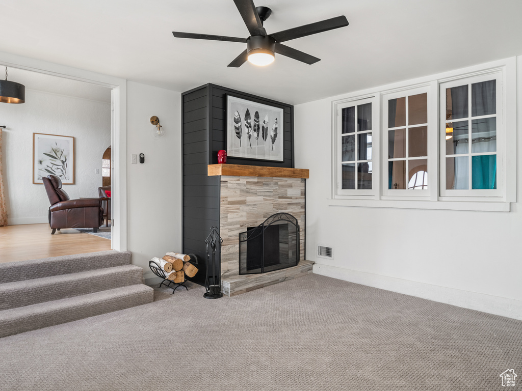Carpeted living room with a tiled fireplace and ceiling fan
