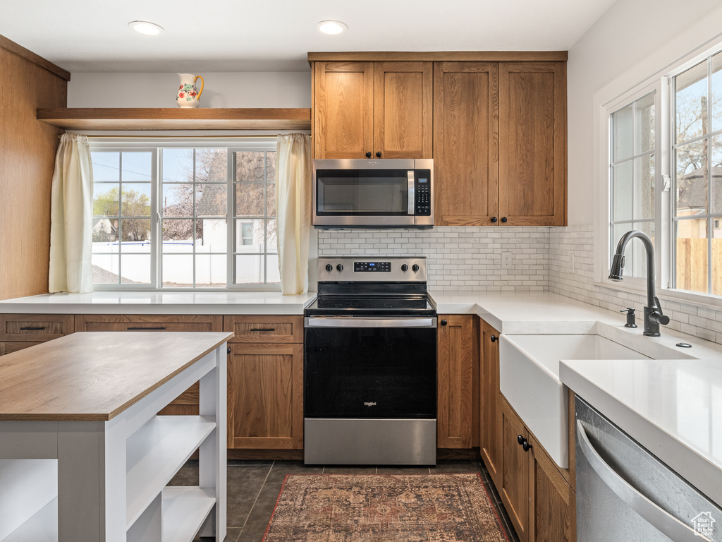 Kitchen featuring appliances with stainless steel finishes, dark tile flooring, tasteful backsplash, and sink