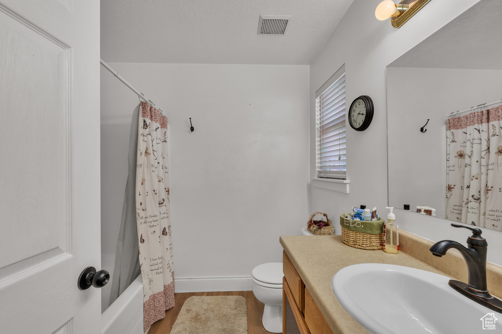 Full bathroom featuring wood-type flooring, shower / tub combo with curtain, vanity, and toilet