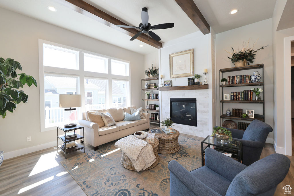 Living room featuring dark wood-type flooring, beam ceiling, ceiling fan, and a fireplace