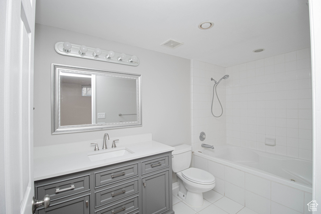 Full bathroom featuring vanity with extensive cabinet space, tiled shower / bath combo, tile floors, and toilet