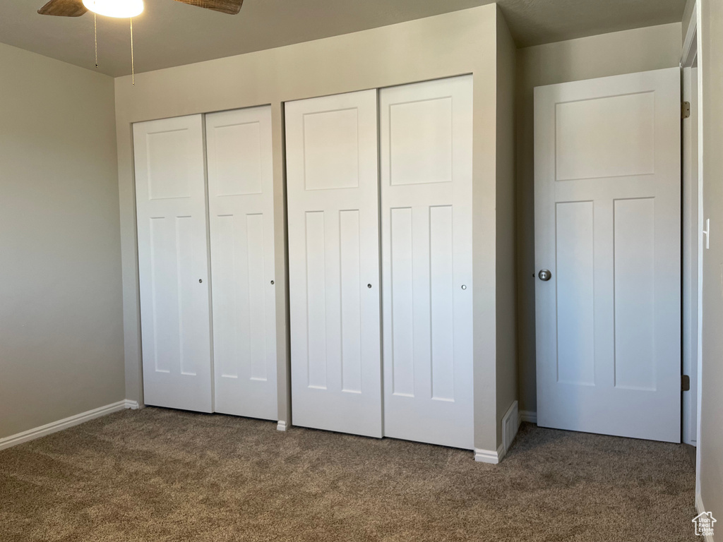 Unfurnished bedroom featuring dark colored carpet, multiple closets, and ceiling fan