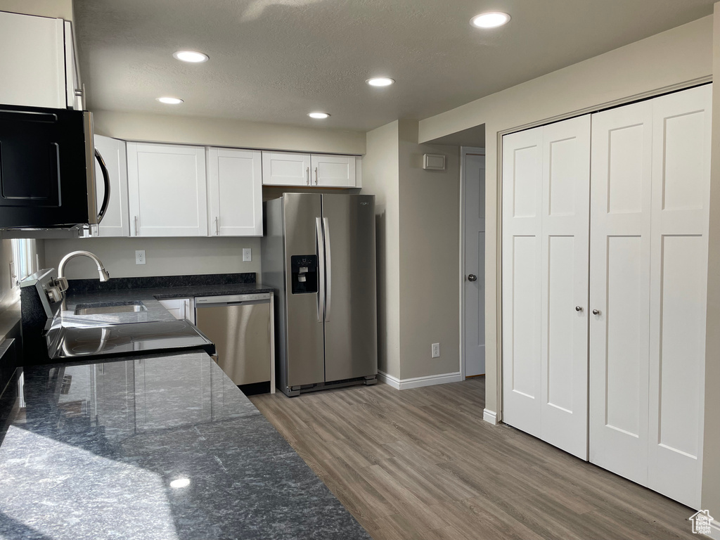Kitchen with white cabinets, hardwood / wood-style flooring, and stainless steel appliances