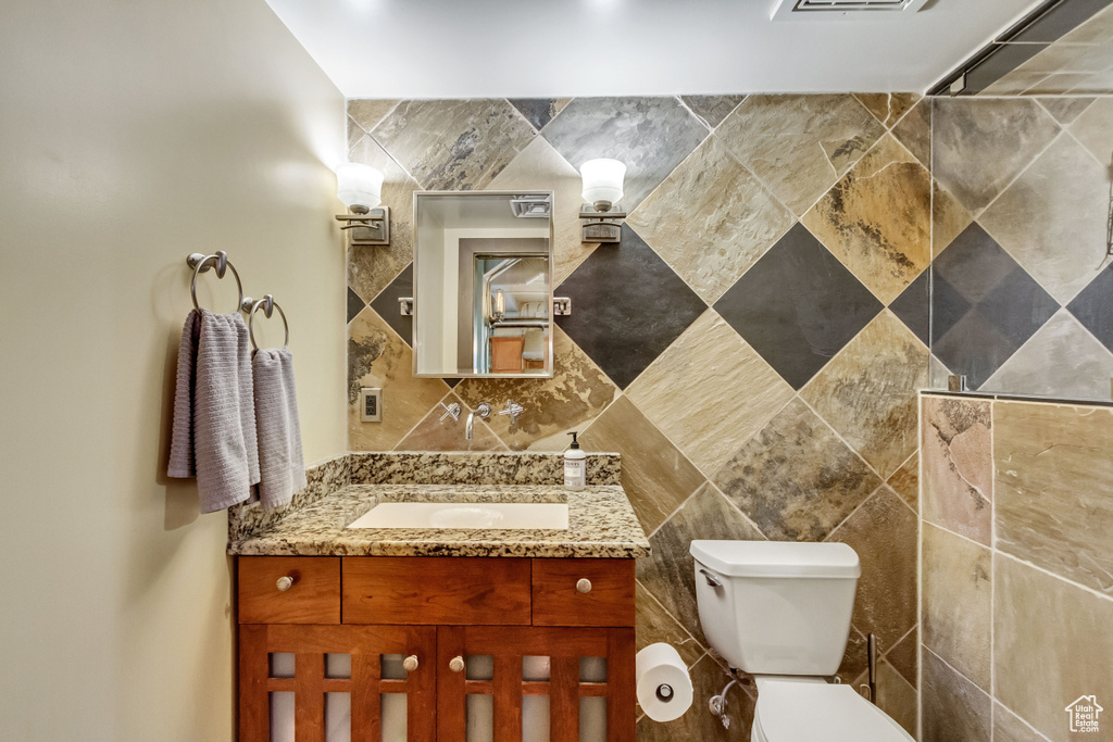 Bathroom featuring vanity, toilet, and tile walls