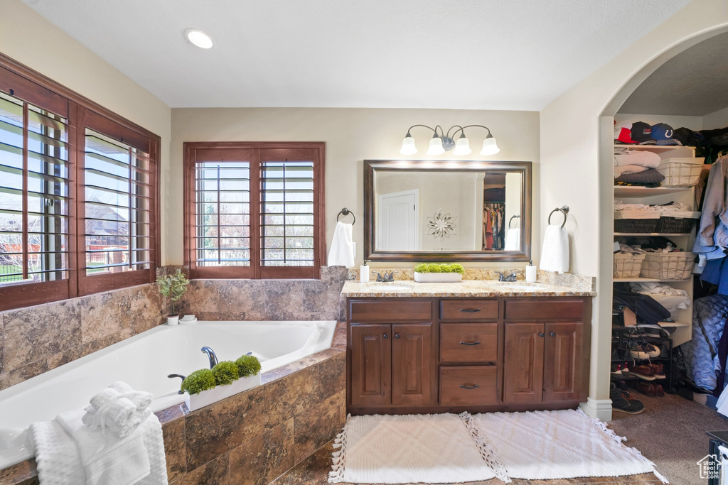 Bathroom featuring dual sinks, tiled tub, and large vanity