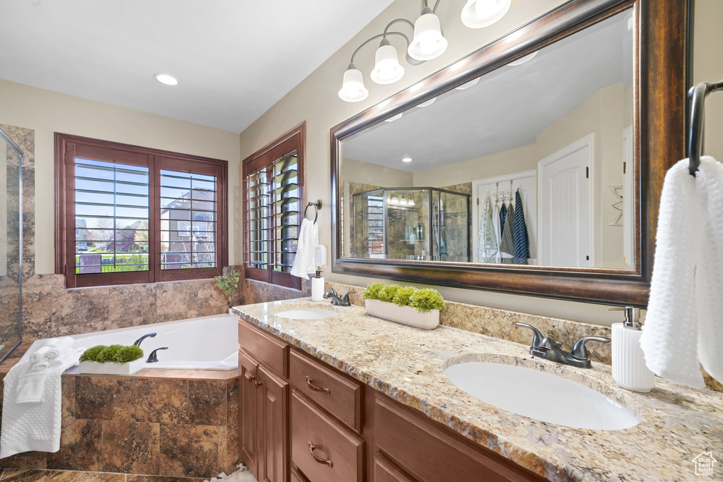 Bathroom featuring vanity with extensive cabinet space, double sink, and plus walk in shower