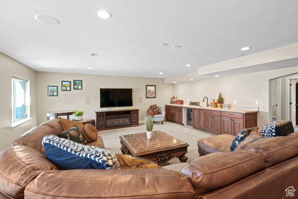Living room featuring a textured ceiling, sink, light carpet, and wine cooler