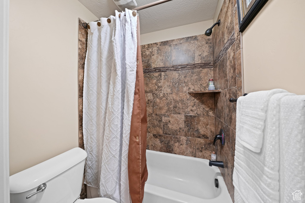 Bathroom featuring toilet, shower / bath combo with shower curtain, and a textured ceiling