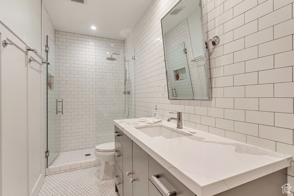 Bathroom with tile walls, walk in shower, toilet, vanity with extensive cabinet space, and tasteful backsplash