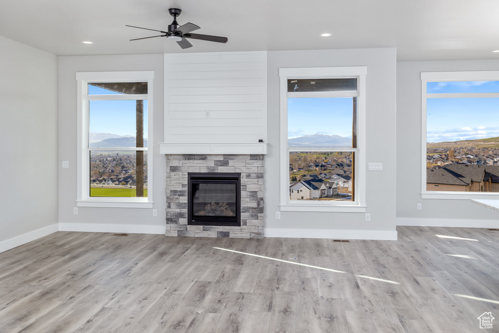 Unfurnished living room with ceiling fan, a mountain view, light wood-type flooring, and a stone fireplace