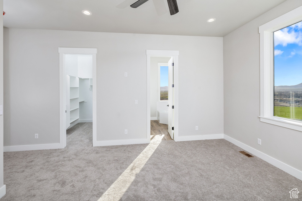 Unfurnished bedroom featuring ceiling fan, light carpet, a closet, a walk in closet, and connected bathroom