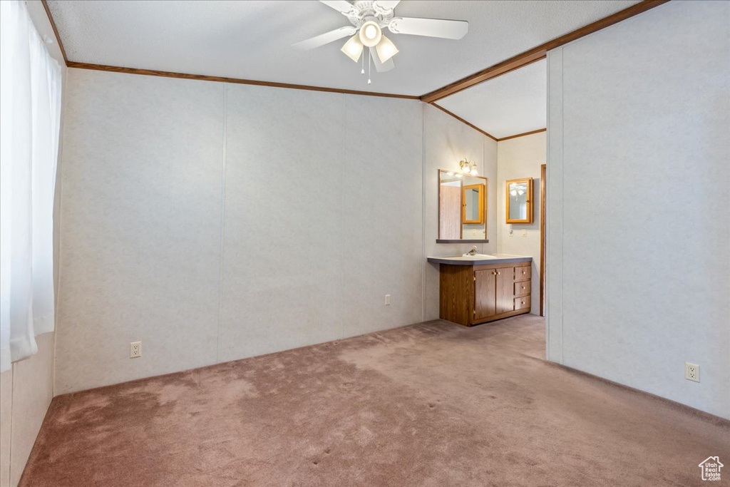 Unfurnished bedroom with light colored carpet, ceiling fan, vaulted ceiling, sink, and ornamental molding