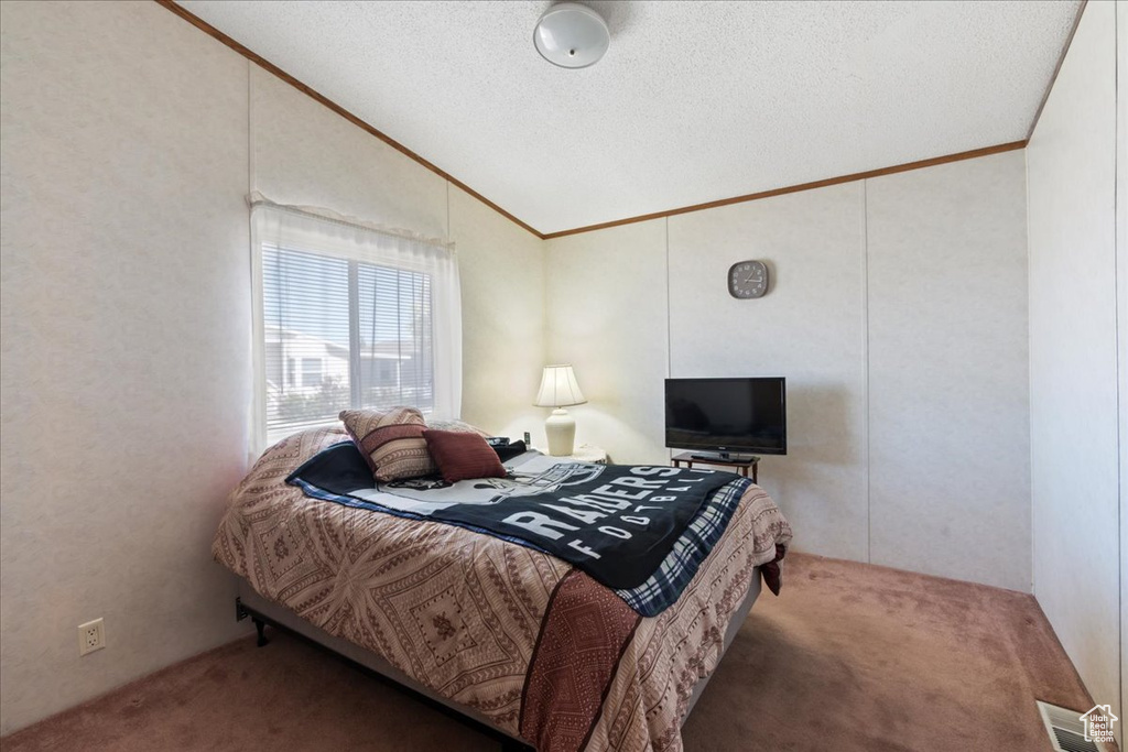 Bedroom featuring lofted ceiling, crown molding, carpet floors, and a textured ceiling