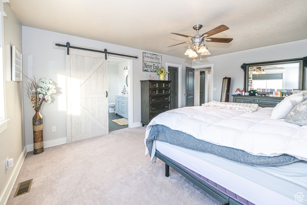 Carpeted bedroom featuring a barn door, connected bathroom, and ceiling fan