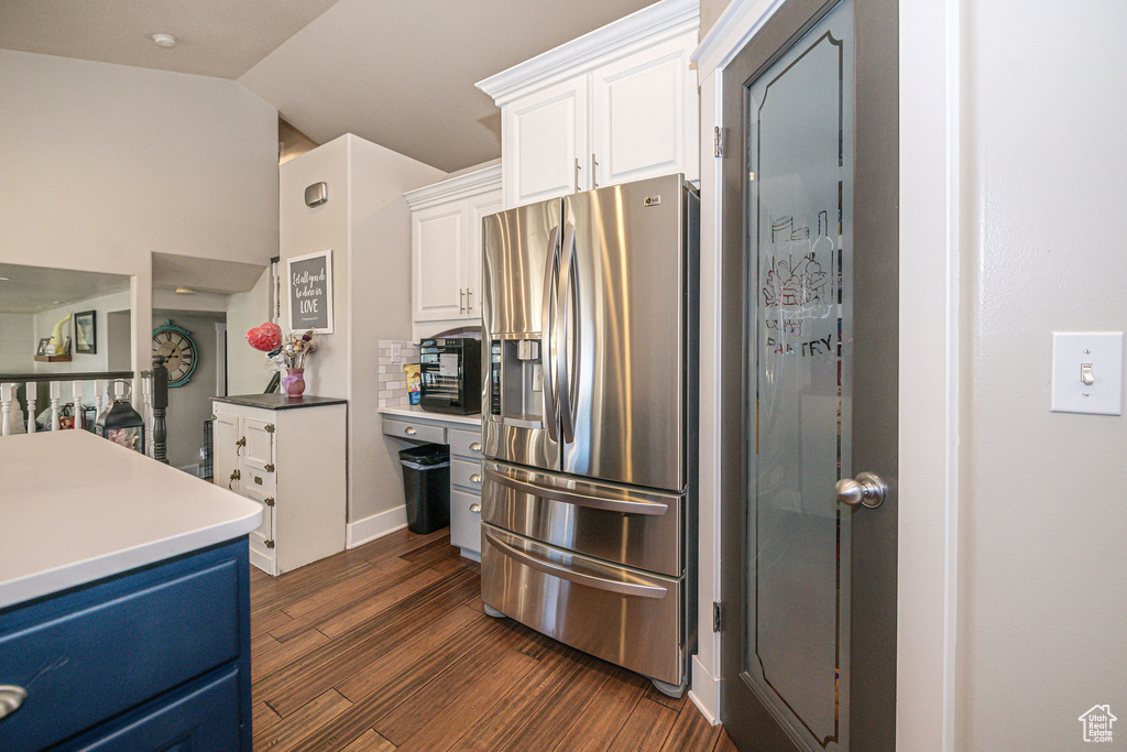 Kitchen featuring backsplash, stainless steel fridge, vaulted ceiling, white cabinetry, and dark hardwood / wood-style flooring
