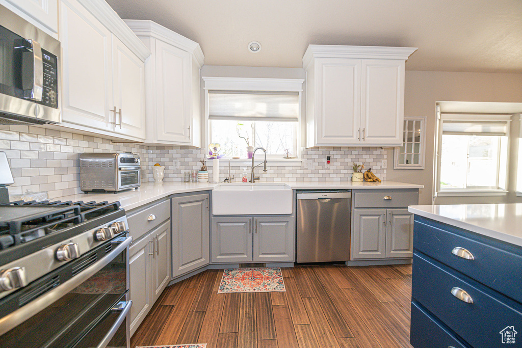 Kitchen with stainless steel appliances, tasteful backsplash, white cabinets, sink, and dark hardwood / wood-style flooring