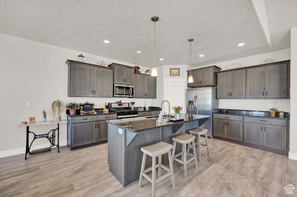 Kitchen with appliances with stainless steel finishes, sink, light hardwood / wood-style floors, a breakfast bar area, and decorative light fixtures