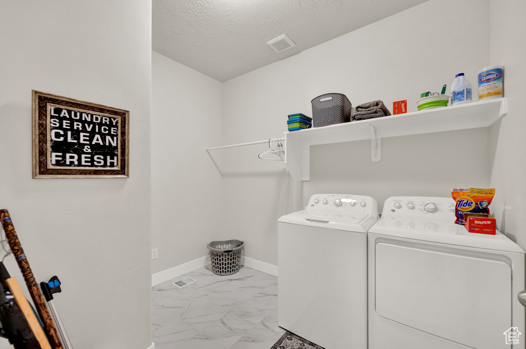 Laundry room with washing machine and dryer, light tile floors, and a textured ceiling