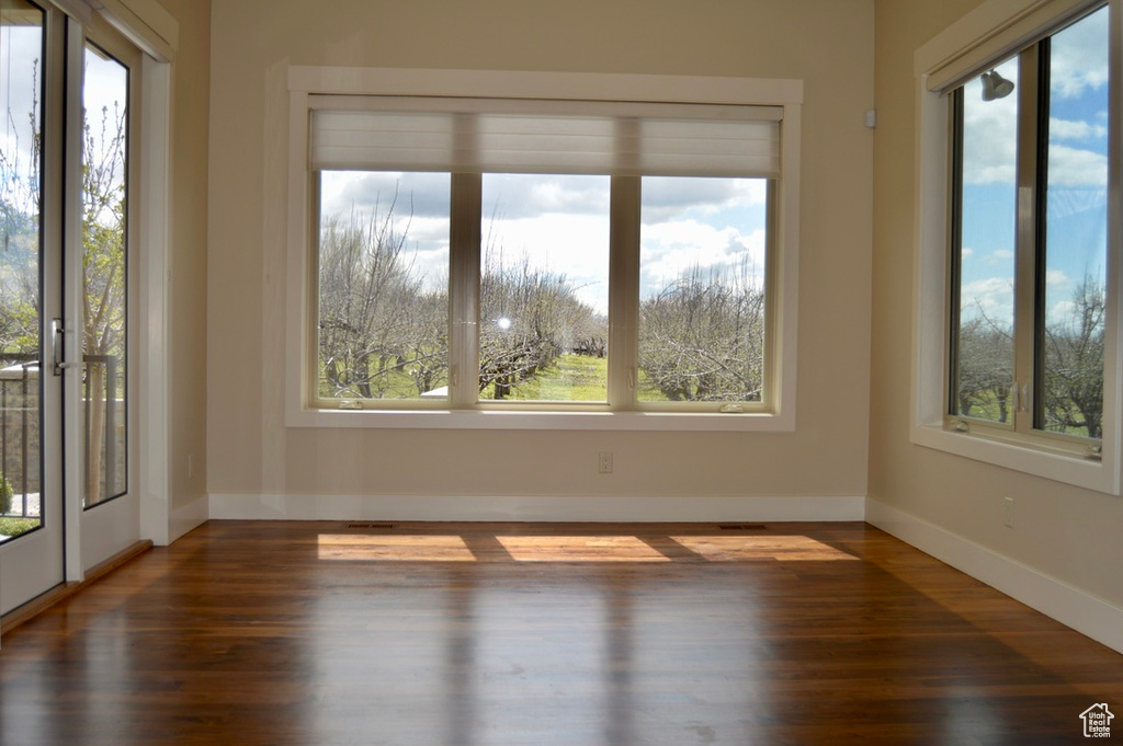 Empty room with dark hardwood / wood-style floors and a healthy amount of sunlight