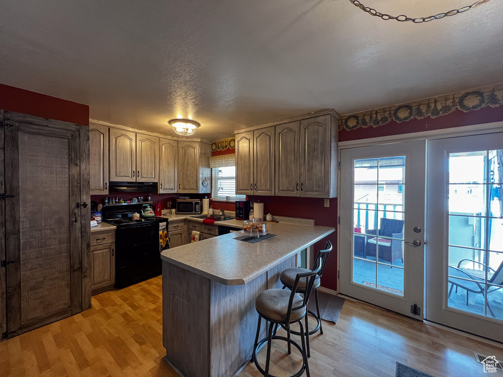Kitchen featuring black electric range oven, light hardwood / wood-style flooring, kitchen peninsula, and a breakfast bar