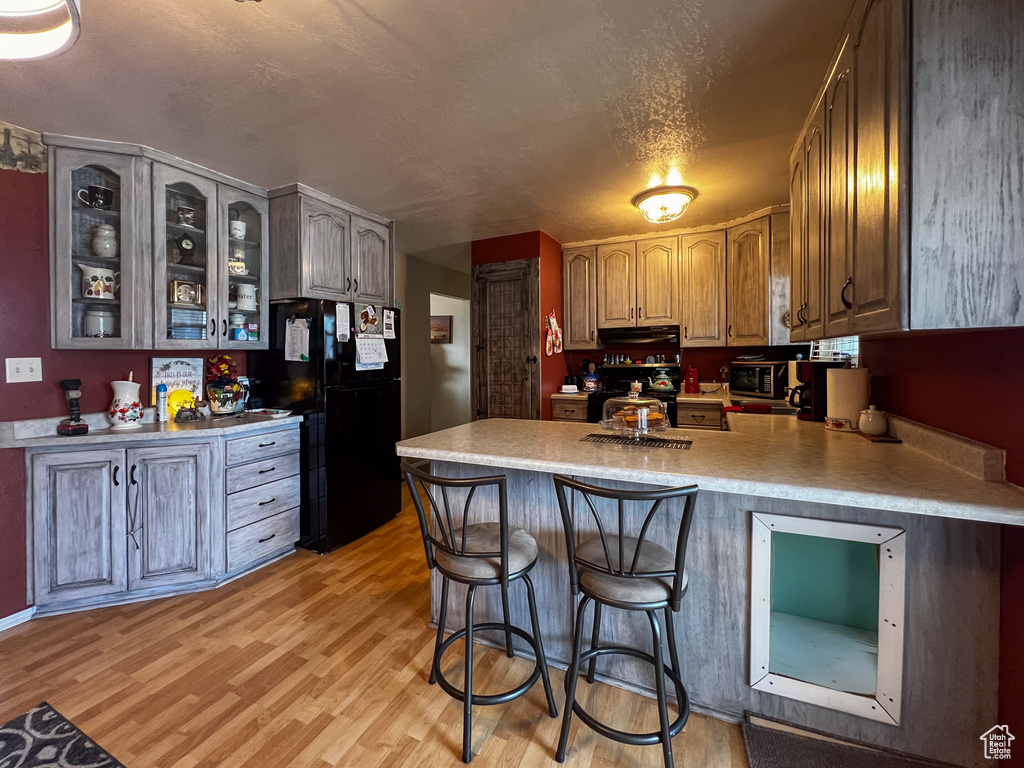 Kitchen featuring range, black refrigerator, light hardwood / wood-style flooring, kitchen peninsula, and a kitchen breakfast bar