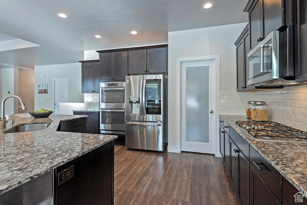 Kitchen featuring sink, backsplash, stainless steel appliances, dark hardwood / wood-style floors, and light stone countertops