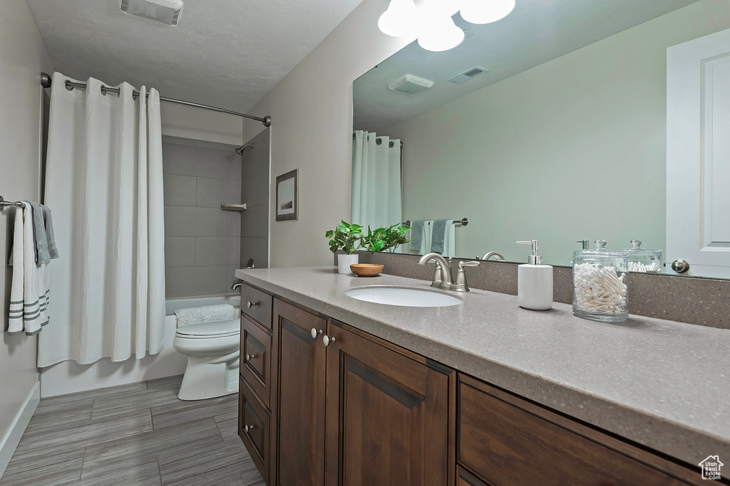 Full bathroom featuring a textured ceiling, oversized vanity, shower / bath combination with curtain, tile floors, and toilet