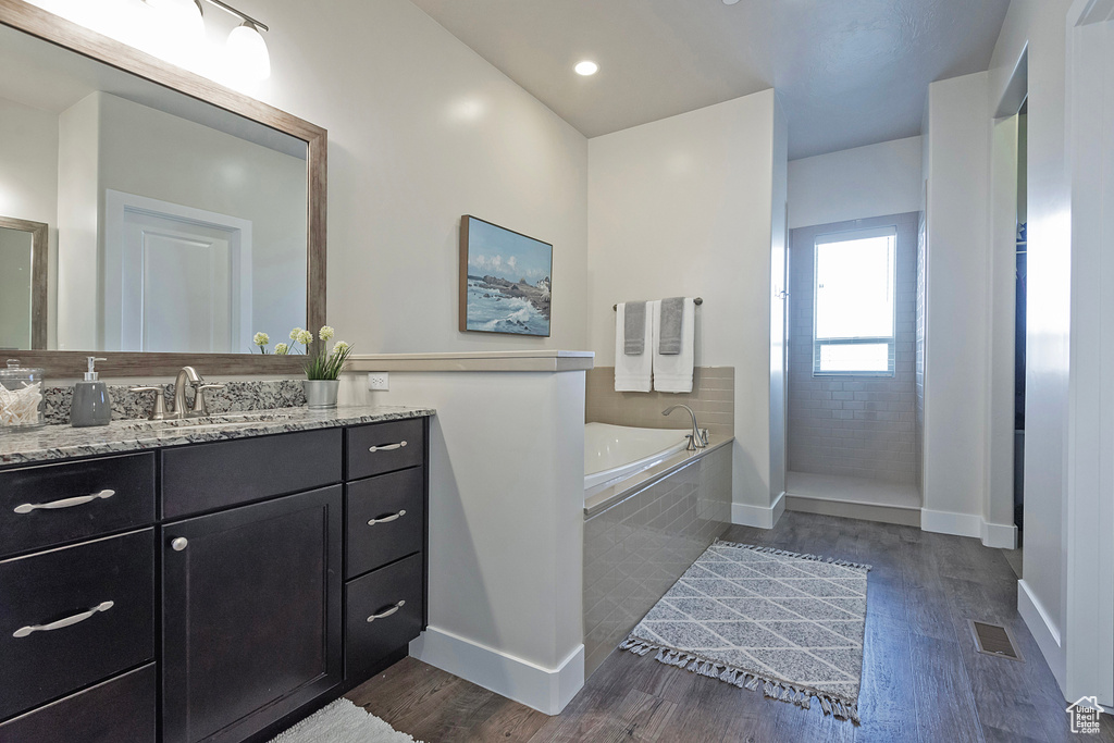 Bathroom with hardwood / wood-style floors, vanity, and a relaxing tiled bath