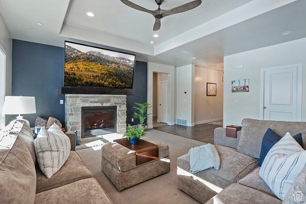 Living room with hardwood / wood-style floors, ceiling fan, a stone fireplace, and a tray ceiling