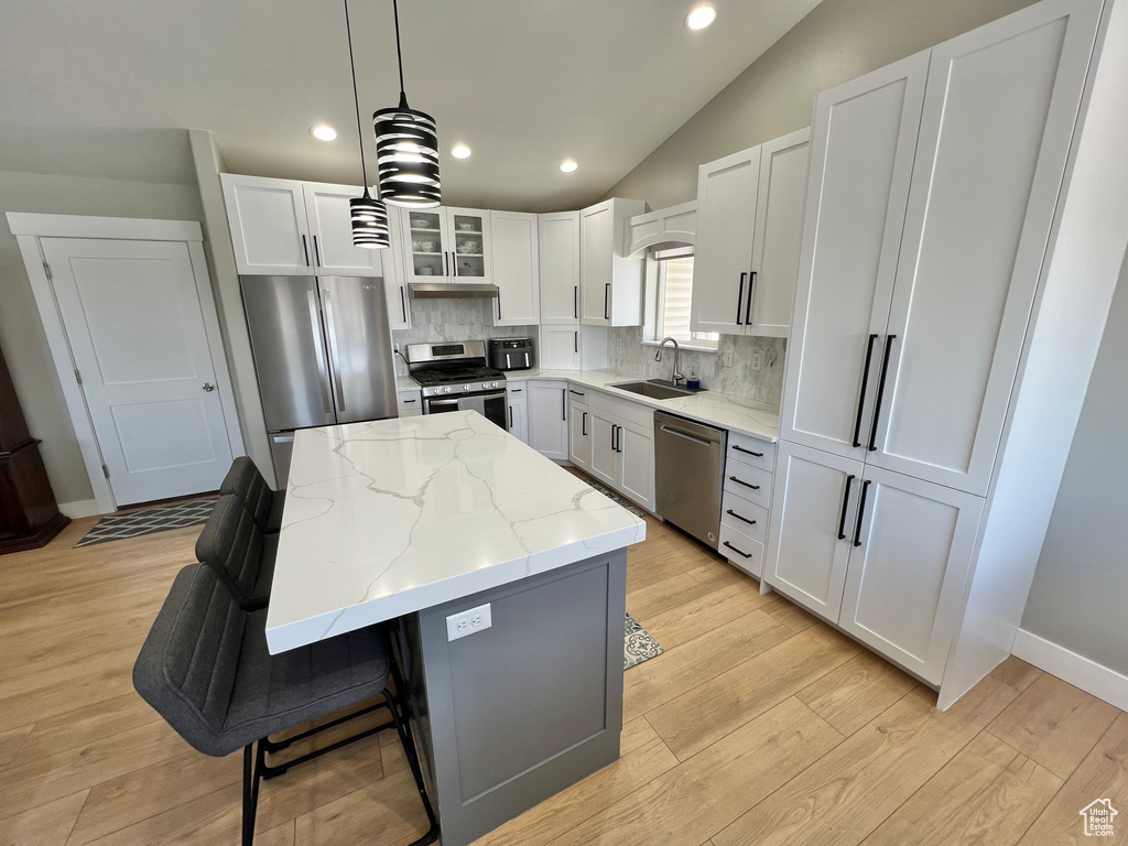 Kitchen with appliances with stainless steel finishes, white cabinets, backsplash, light hardwood / wood-style flooring, and pendant lighting